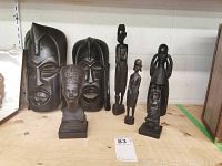 Photo showing the entire lot of two wooden masks and five carved wooden figures on a wooden table.