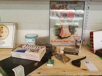 Photo showing full lot setup on wooden shelf with tobacco tins, matchboxes, lighters, and advertising sign visible