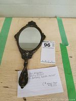Front view of the oval mirror with handle laid flat on a table, showing the reflective mirror surface and the brass edges.