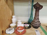 Full view of shelf with porcelain tea cups, lidded dish, small vases, and tall decorative glass vases