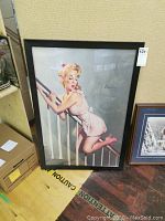 Full view of the framed print of a pin-up girl on a staircase railing.
