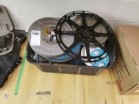 Plastic basket filled with assorted metal and plastic film reels including Kodak branded metal case on top, showing wear.