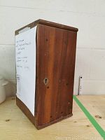 Closed wooden storage case with keyhole showing the exterior of the vintage microscope storage box.