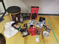 Wide view of full lot showing Elvis Presley tin, T-shirt, Pepsi bottle, CD set, license plate, ashtray, coasters, plush bear, cards and pins.