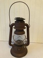 Front view of the vintage metal lantern showing the rust-colored metal frame and clear embossed glass globe.