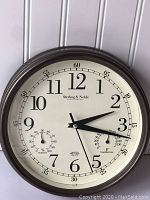 Full view of wall clock showing brand Sterling & Noble, analog clock face with hour, minute, and second hands, and two smaller dials for temperature and humidity.