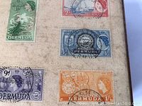 Close-up of several different used Bermuda stamps attached to the box lid showing postmarks and different colors and denominations.