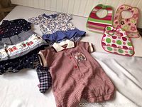 Four baby girls outfits and three bibs displayed on floor