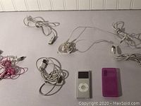 Top view of silver iPod Classic, white earbud headphones, and four charging cables laid out on white surface.
