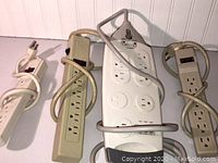 Four assorted electrical power strips arranged on a surface, showing cords and outlet configurations