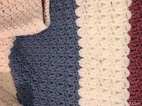 Close-up of blanket yarn and crochet pattern showing cream and blue stripes with textured stitches.