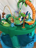 Evenflo Exersaucer Triple Fun activity center with green base, blue supporting legs, and various colorful toys attached, designed for infant play and development.