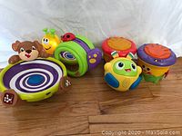 Lot of six Fisher Price infant toys including drums, animal themed musical toys, and activity toys, displayed on a wooden surface.