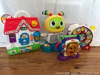 Four baby toys including a Fisher-Price Laugh and Learn house, a musical caterpillar, a flip book toy, and a baby piano.