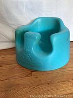Blue Bumbo infant floor seat on wooden floor, showing front and side with embossed Bumbo logo and elephant design.