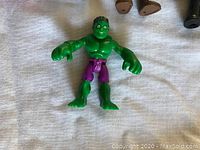 Single Hulk action figure with green skin and purple pants, lying on white cloth surface.
