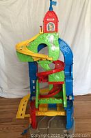 Front view of multi-level colorful car ramp toy with red tower topped by a blue flag and various ramps including red and yellow spiral paths.