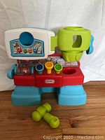 Front view of the Little Tikes toy work bench showing colorful knobs, ABC decals, and two small green toy tools in front.