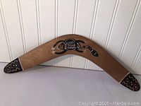 Wooden boomerang showing overall shape and painted Aboriginal style lizard design on wood surface.