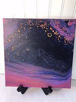 Front view of a 12" x 12" square canvas acrylic pour painting with dark purples, pinks, and copper detail mounted on a black easel.