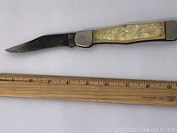 Full view of the vintage folding pocket knife with blade extended, placed beside a ruler showing approximately 9 inches in length
