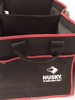 Photo showing front of Husky collapsible tote with black fabric and red trim, includes front pocket with Husky logo and text.