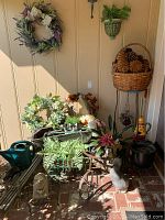 Photo showing plant carts, planter pots with artificial flowers, garden statues, watering jug, broom, and a display bench in sunlight.
