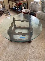 Round coffee table with clear glass top and dark carved wooden base on carpet.