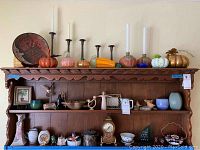 Wide view of wooden shelf displaying candle holders, glass vase, ceramic art, mini clock, decorative plates and small ceramics