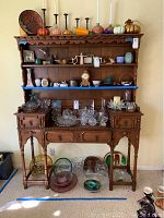 Front view of vintage wooden hutch with three shelves, decorative items on shelves, two side drawers with ornate legs.