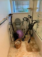 Photo of corner with multiple mobility aids: walkers, canes, crutches, a commode chair, exercise ball, and waste baskets.