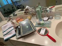 Overview of all items on the bathroom counter including trays, soaps, jar, bottles, mirror, and toothbrush holder.
