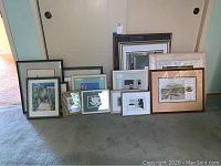 Seventeen framed wall art pieces arranged leaning against wall, showing size range and frame variety