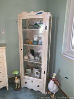 Full view of white cabinet containing multiple items - ceramic rabbits, ducks, glass art, plate, picture frames, vases, faux plants visible inside and on shelves.