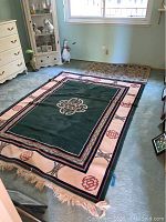View showing both rugs in a room, larger green and pink bordered rug in foreground and smaller brown floral rug near window