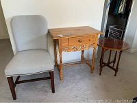 Photo showing upholstered chair, rectangular end table with drawer and carved apron, and small round end table