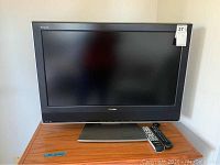 Full view of Toshiba 32-inch flatscreen TV on a wooden surface with two remote controls placed on the base of the TV.