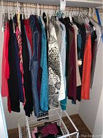 Long view of women's tops and pants hung on hangers on a rod, various colors and patterns visible.