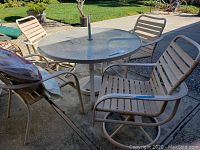 Photo of outdoor patio table with round glass top and four chairs around it on concrete patio