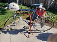 Full side view of the men's Centurion Le Mans 12 road bike showing blue frame, drop handlebars, rear rack, red saddlebag, white helmet on handlebars, and red pump beside the bike.