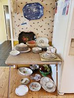Full view of lot with dishes stacked on table, faux fruit in basket and bowls, decorative trays on wall and table