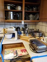 Overview of kitchen counter and cupboards showing vintage stand mixer, pots, pans, waffle irons, towels, and other kitchen items.