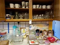 Kitchen counter with clear glass baking dishes, glassware including cups, mugs, and glasses arranged on and inside a wooden cabinet.