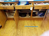 Open lower cabinets showing metal and glass baking pans, plastic storage containers, and folded linens.