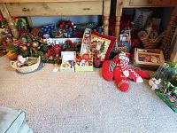 Wide view of assorted Christmas decorations, bows, and holiday wrapping materials arranged under a wooden piece of furniture.