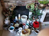 Photo showing arrangement of faux plants, vases and pots including a variety of ceramic and glass pots, and the metal plant stand with a bronze-colored pot.