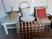 Overview of two wooden side tables, three woven baskets (two placed on a table and one standing), a wooden wine rack in front, wicker chair with red throw pillow beside the tables.