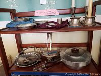 Three-tier shelf with sterling silver items on top shelf and silver-plated pieces on bottom shelf