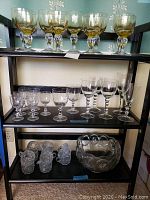 Shelf display of punch bowl and various glasses, including clear stemware and amber stemmed glasses, plus punch cups on bottom shelf.