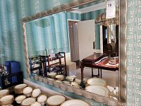 Full view of the large rectangular mirror mounted on a patterned blue wallpaper wall reflecting dining area and tableware.